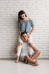 Woman stands before a white wall while her man sits beneath her feet