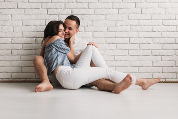Tender hugs and kisses of man and woman resting on the floor in white room
