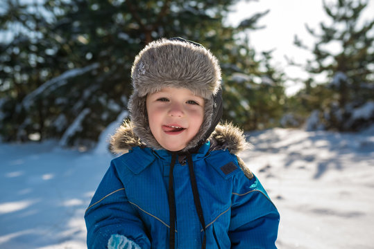 Happy cute little boy dressed in warm coverall and hat in winter frozen snowy forest