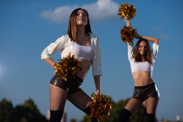 Two girls cheerleaders with pompons dancing outdoors