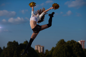 cheerleader girl with pompoms performs acrobatic elements outdoors on sky background