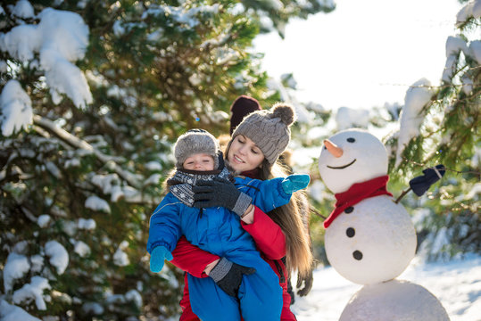 Happy young mother and her son have fun in winter. Play in snow and make snowman