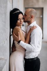 Handsome young bald headed man hugs with passion young brunette in pink evening dress