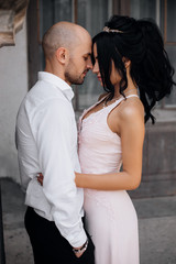 Handsome young bald headed man hugs with passion young brunette in pink evening dress