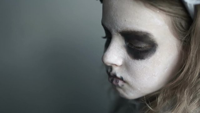 Close portrait of a girl in the makeup of a dead man. White face, black circles around the eyes, black lips. Portrait for Halloween. Creative celebration of the day of the dead, cold colors