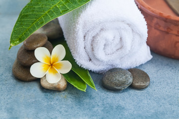 Obraz na płótnie Canvas Tropical flower, white towel and stones for spa massage on blue
