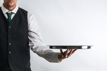Butler / waiter in white shirt and black suit vest carrying an empty silver tray. Copy space for...