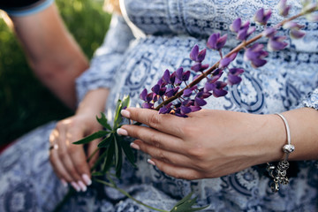 Fototapeta premium Man and pregnant woman sit together in a green grass full of violet lavander flowers