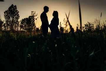 Silhouettes of man and pregnant woman standing on the field in rays of evening sun