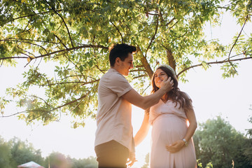Man hugs beautiful pregnant woman tender standing before the lake in the rays of evening sun