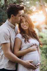 Fototapeta premium Man hugs beautiful pregnant woman tender standing before the lake in the rays of evening sun