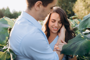 Cheerful man and pregnant woman hug each other tender standing in the field with tall sunflowers around them
