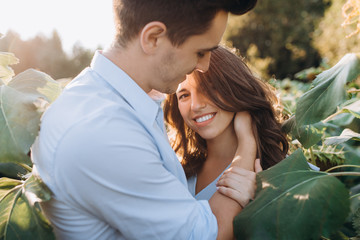 Cheerful man and pregnant woman hug each other tender standing in the field with tall sunflowers around them