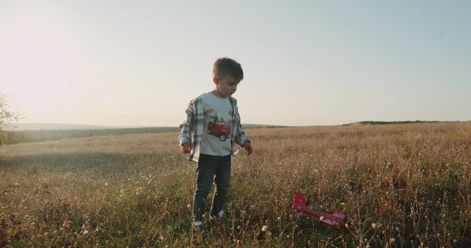 Dreaming little charismatic boy , playing with a airplane , jumping in the middle of field. slow motions