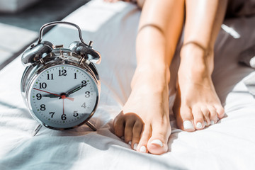 close-up partial view of female feet and alarm clock on bed