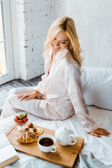 high angle view of smiling beautiful woman looking at wooden tray with breakfast in bed in morning - obrazy, fototapety, plakaty