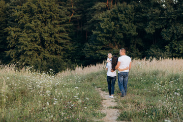 Naklejka na ściany i meble Warm hugs of young parents and their little daughter standing in the summer field