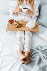 Fototapeta na wymiar cropped image of woman in pajamas having breakfast in bed in morning