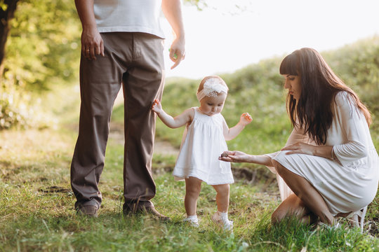 Young parents walk with their lovely little daughter in jeans dress across the field