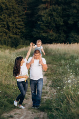Warm hugs of young parents and their little daughter standing in the summer field