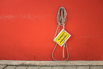 Aufgehängtes Schild Ausfahrt freihalten an Seil vor orangeroter Hauswand