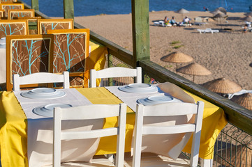 Cafe on the public beach.. A row of white tables with yelow tablecloths and dishes.  The coast of the Aegean Sea. Turgusreis, Bodrum, Turkey