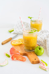 still life of apple grapefruit fresh juice in glass cups on a wooden board on a white background with slices of fruit