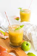 still life of apple grapefruit fresh juice in glass cups on a wooden board on a white background with fruit slices close-up