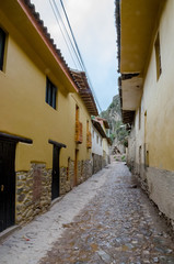 Obraz premium Ancient stone street with colonial buildings in a rainy day with mountains in the back at Ollantaytambo town, Peru