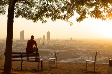 Man on a bench relaxing and enjoying the summer sunrise over a city. Lyon, France.