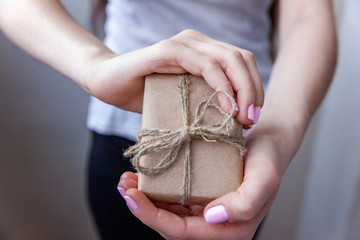 Female hands holding small gift box wrapped craft paper with ribbon. Small christmas or new year...