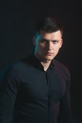 Man with serious young face on dark backgroud. Man wear fashionable black shirt