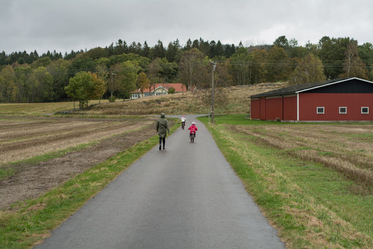 A girl in a rain jacket is out walking while her children riding their bicycles