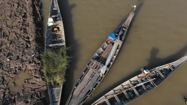 Aerial slow motion (60fps) from left to right across small wooden fishing boats in rural Cambodia, Southeast Asia. Muddy shore is partly visible