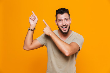 Emotional young happy man posing isolated over yellow background pointing.