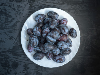 white plate with ripe prunes on a dark wooden background