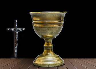 Old chalice on wooden table next to an iron Cross