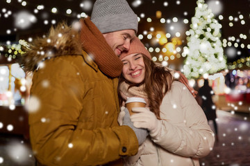 winter holidays, hot drinks and people concept - happy young couple with coffee at christmas market in evening