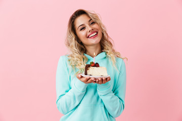 Photo of happy woman in basic clothing holding piece of birthday cake with candle, isolated over...