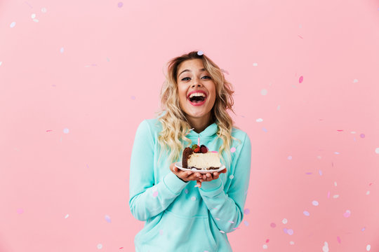 Photo of pretty woman in basic clothing holding piece of birthday cake with candle, isolated over pink background