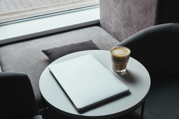 high angle view of laptop and cup of cappuccino on table in coffee shop