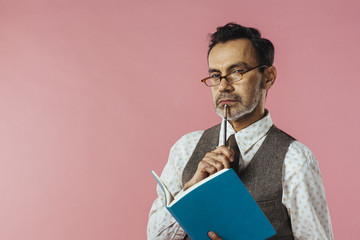 Portrait of an older teacher with pen and notebook, looking over his glasses