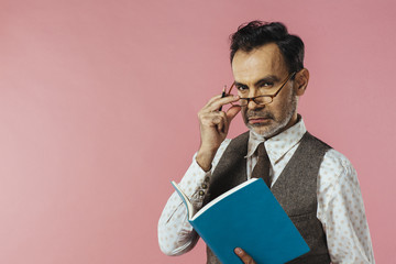 Portrait of  a mature man in vest holding notebook, glasses and notebook, isolated on pink
