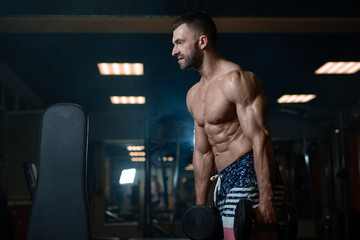Fototapeta na wymiar young muscular man posing with dumbbells in hand at the gym
