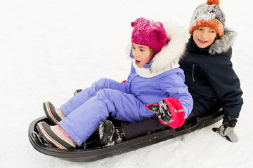 childhood, sledging and season concept - happy little kids sliding on sled down snow hill in winter