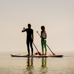 Silhouette of young happy couple doing paddle yoga