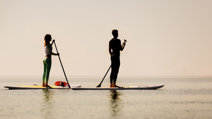 Young couple doing sup yoga on sunset background