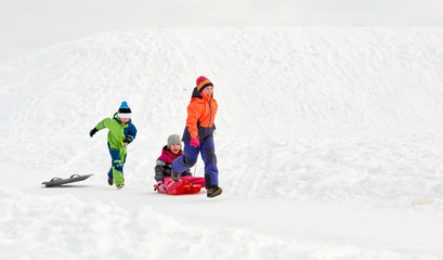 childhood, leisure and season concept - group of happy little kids in winter clothes with sled having fun outdoors