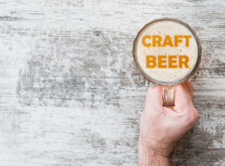 man's hand holds a mug of beer with silhouettes of word "craft beer". Top view. Space for text