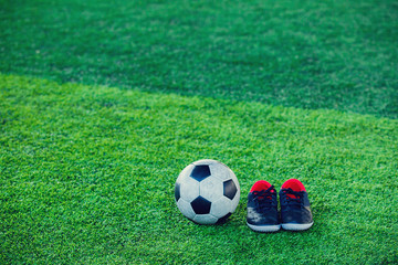 Fototapeta na wymiar Football and black red sports shoes on green artificial turf